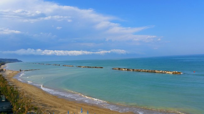 Spiaggia con mare calmo e dighe frangiflutti sotto un cielo coperto.