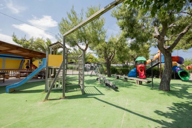 Un parco giochi con scivolo blu e altalene circondato da alberi.