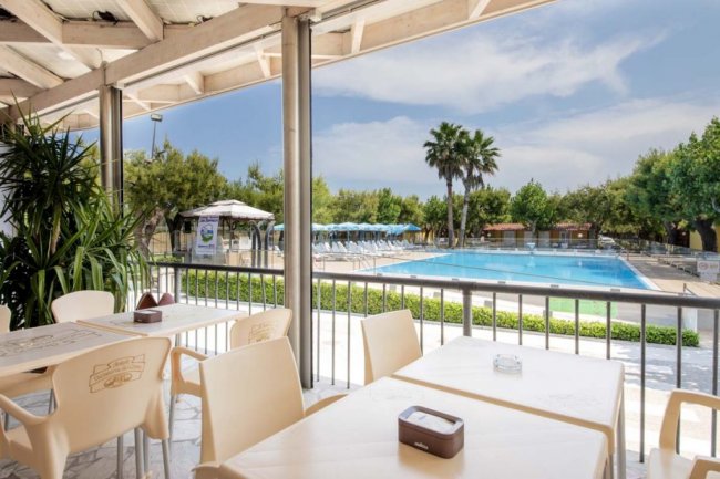 Tavoli di un ristorante con vista su una piscina blu e alberi circostanti.