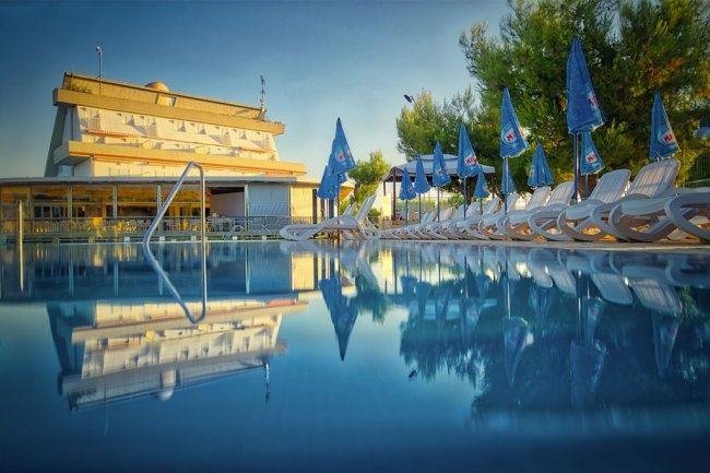 Piscina con lettini e ombrelloni blu accanto a un edificio.