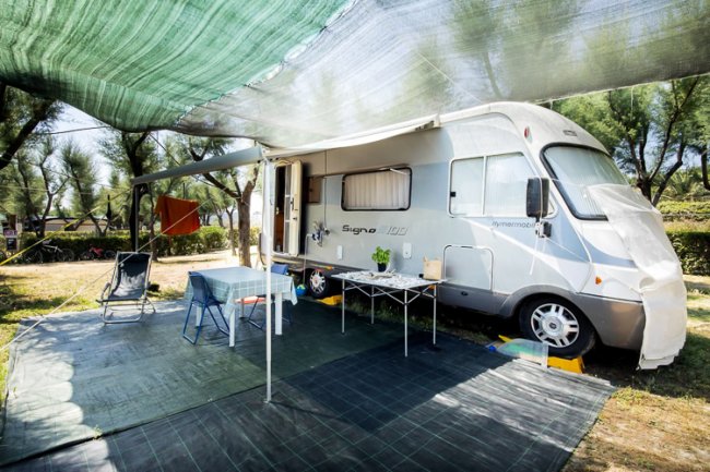 Camper parcheggiato con tavolo, sedie e tenda ombreggiante.
