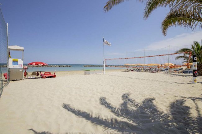 Spiaggia con rete da pallavolo, ombrelloni arancioni e bandiere, vicino al mare.