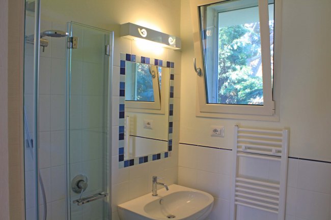 Bagno con doccia in vetro, specchio con piastrelle blu e finestra.