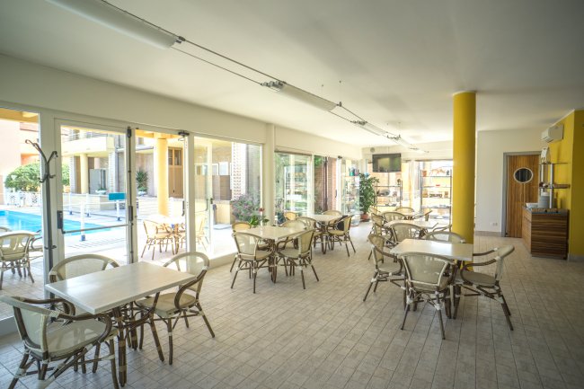Sala da pranzo luminosa con tavoli e sedie vicino a grandi finestre.