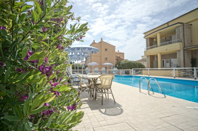 Tavolini e sedie accanto a una piscina, con cespugli fioriti a sinistra.