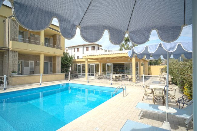 Piscina all'aperto con ombrelloni blu e un edificio giallo sullo sfondo.