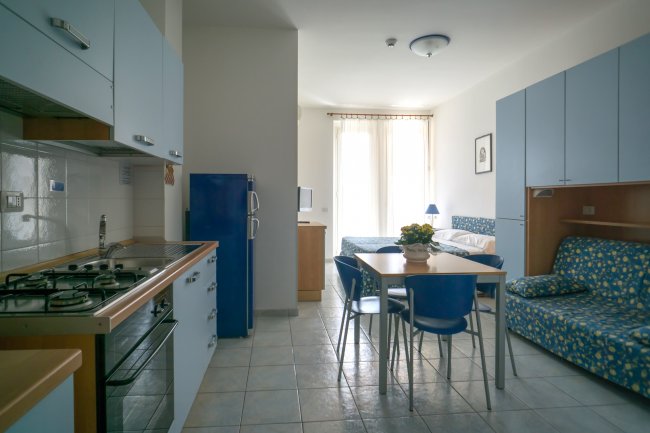 Interno appartamento con cucina blu, tavolo e divano-letto a fantasia.