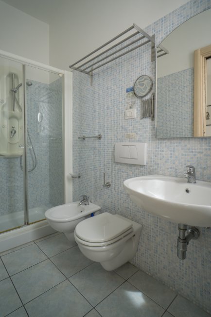 Bagno con doccia in vetro, lavabo, wc e bidet. Pavimento e pareti con piastrelle chiare.