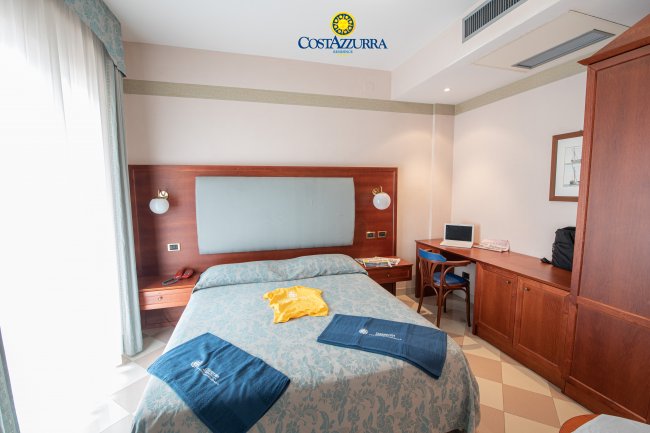 Camera da letto con letto matrimoniale, scrivania e asciugamani blu su una coperta.