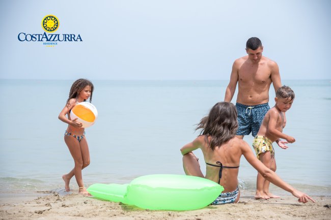 Famiglia in spiaggia, due adulti e due bambini giocano sulla sabbia vicino al mare.
