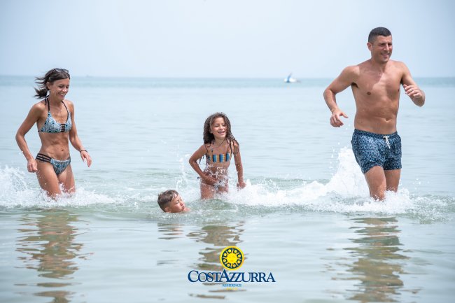 Una famiglia gioca nell'acqua al mare, sorridendo e correndo.