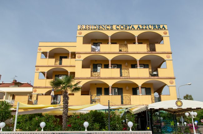 Edificio del Residence Costa Azzurra, giallo con balconi e piante davanti.