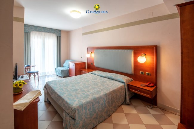 Camera d'hotel accogliente con letto matrimoniale, finestra e poltrona.