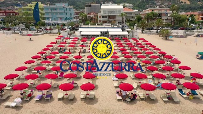 Una spiaggia affollata con file ordinate di ombrelloni rossi e lettini.