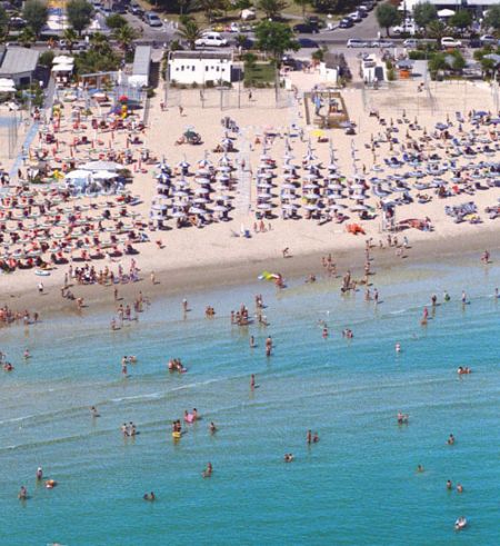 Spiaggia affollata con lettini, ombrelloni e bagnanti nel mare.