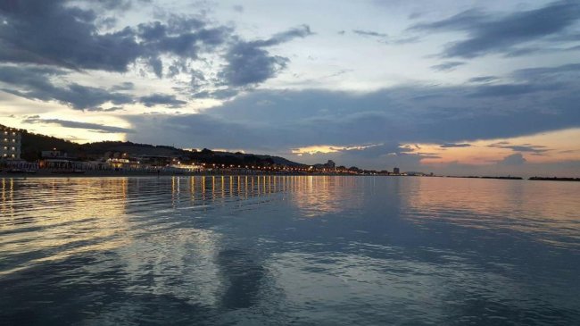 Tramonto su un lungomare con luci riflettenti sull'acqua, cielo nuvoloso.