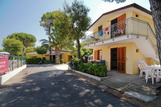 Un edificio a due piani con balcone, circondato da alberi e biciclette parcheggiate.
