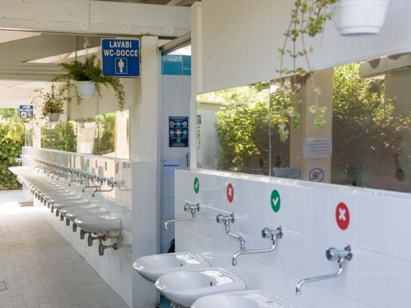 Lavandini con segni di uso corretto, piante sospese e cartelli in un'area bagno esterna.