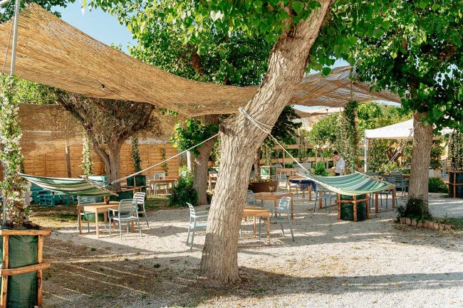 Giardino con tavoli, sedie e amache appese tra gli alberi.