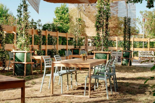 Tavolo all'aperto con sedie in un giardino, circondato da piante rampicanti su grigliati di legno.