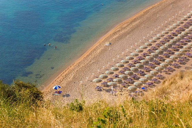 Spiaggia con ombrelloni disposti in file ordinate e poche persone che nuotano nell'acqua.