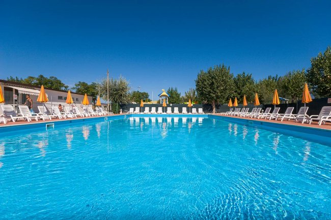 Una grande piscina azzurra circondata da sedie a sdraio bianche e ombrelloni arancioni.