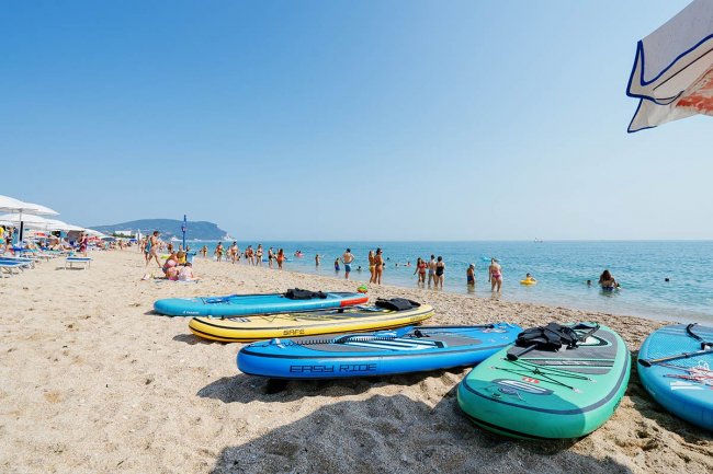 Tavole da surf su una spiaggia affollata con persone che nuotano nel mare.