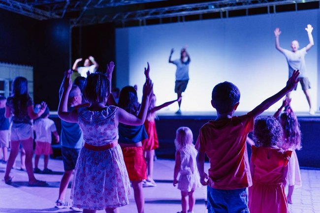 Bambini che danzano di fronte a un palco illuminato di blu.