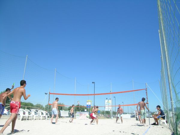 Spiaggia con persone che giocano a pallavolo sotto un cielo azzurro.