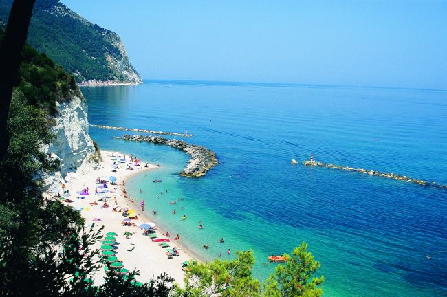 Spiaggia con ombrelloni colorati, mare limpido, e scogliera verde.
