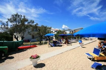 Spiaggia sabbiosa con ombrelloni blu e lettini. Edifici sullo sfondo.