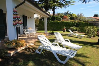 Giardino con sdraio e tavolo sotto un portico vicino a una casa.