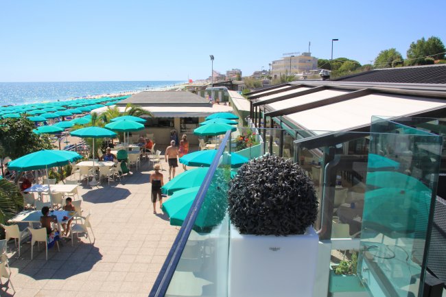Una terrazza sul mare con ombrelloni verdi e tavolini all'aperto.