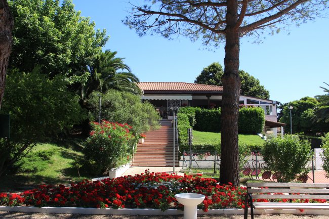 Entrata di un edificio con giardino fiorito e scalinate in legno.