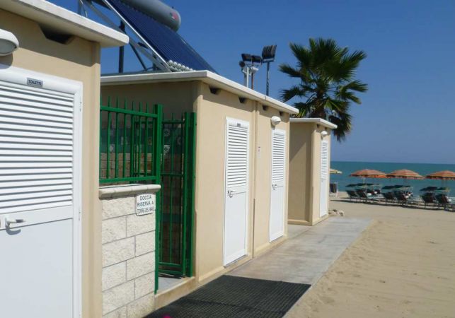 Area docce sulla spiaggia con cabine e ombrelloni sullo sfondo.