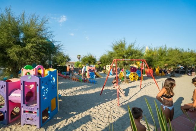Un'area giochi sulla spiaggia con strutture colorate e bambini che giocano nella sabbia.