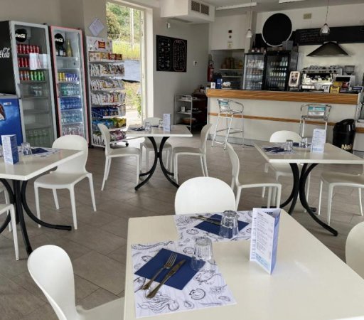 Tavoli e sedie bianche in un bar moderno con frigo e bancone.