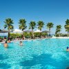 Una piscina con persone che nuotano, ombrelloni e palme sullo sfondo.