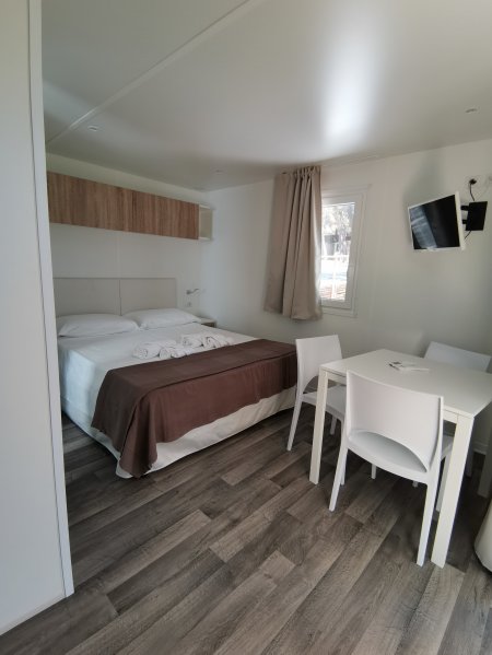 Camera moderna con letto matrimoniale, tavolo e sedie bianche, pavimento in legno.