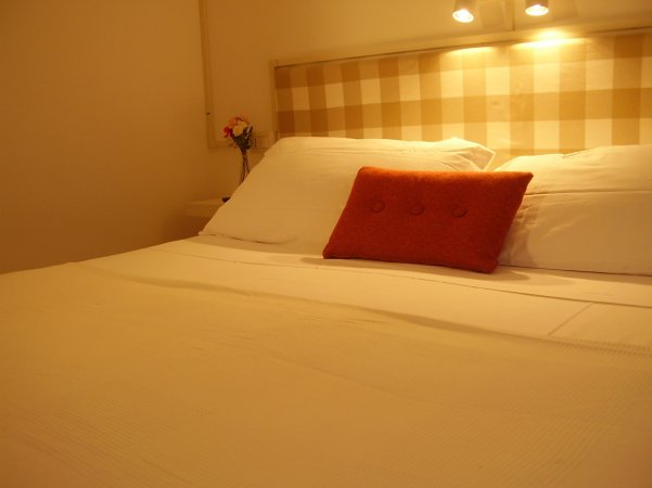 Letto con cuscino arancione, testiera a quadri beige e lampade soffuse.