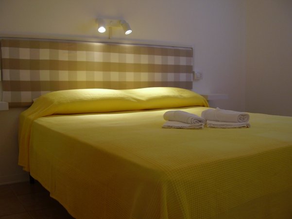 Letto matrimoniale con copriletto giallo e asciugamani arrotolati.
