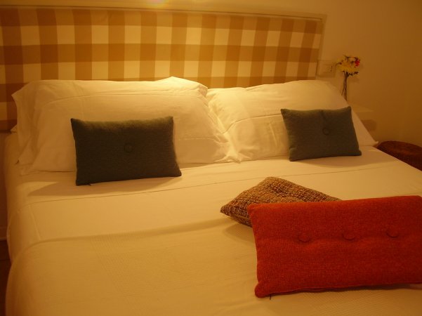 Letto matrimoniale con cuscini blu e rossi, testata a quadri beige.