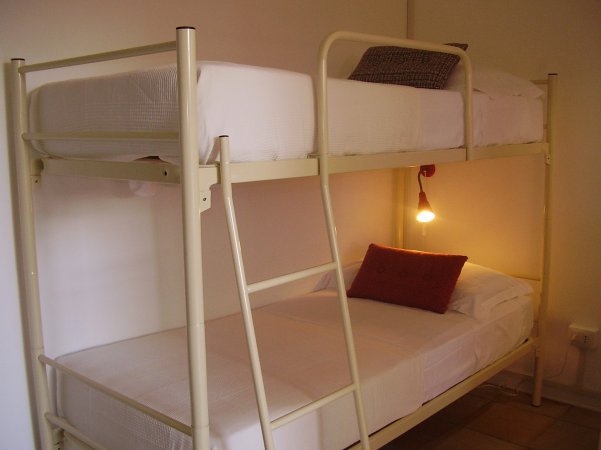 Letto a castello bianco con cuscini, illuminato da una lampada appesa.