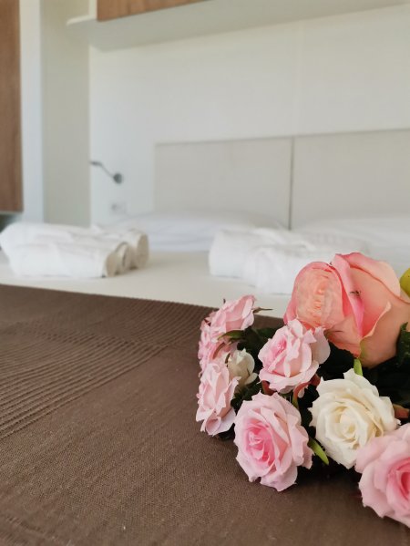 Letto con lenzuola bianche, fiori rosa e asciugamani piegati.