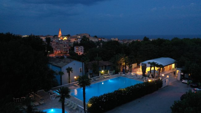 Vista notturna di una piscina illuminata e una città sullo sfondo.