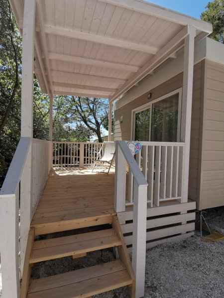 Una veranda in legno con sedie bianche, circondata da alberi.