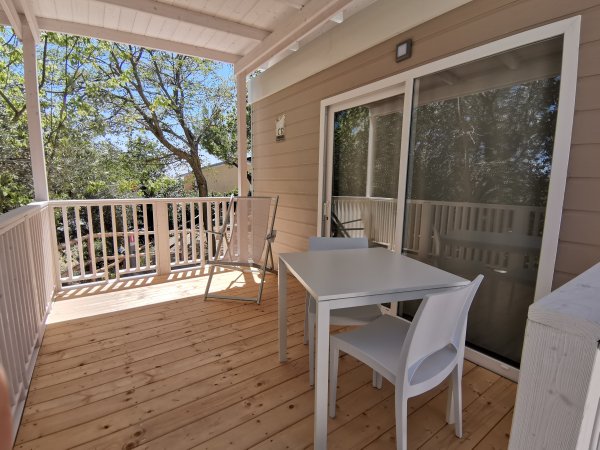 Veranda in legno con tavolo bianco, sedie e vista su alberi.