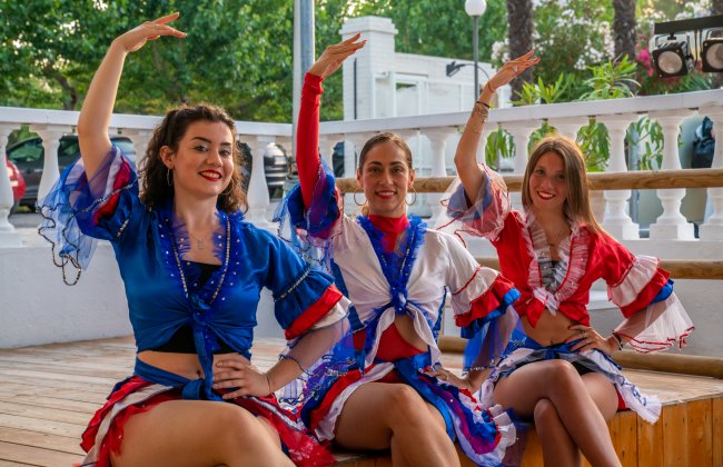 Tre donne in costumi colorati che ballano su un palco di legno.