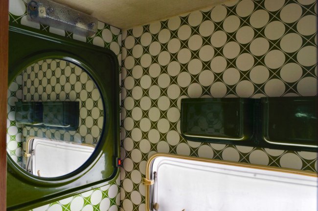 Interno con specchio tondo, pareti piastrellate verdi e bianche.