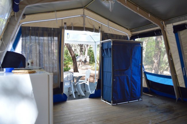Interno di tenda con pavimento in legno, mobili bianchi e sedie all'esterno.